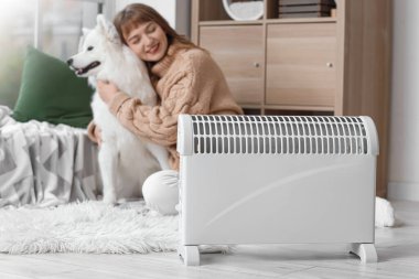 Samoyed köpekli genç kadın radyatörün yanında ısınıyor, yakın plan.