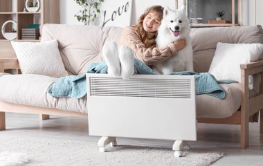 Ekoseli genç bir kadın ve Samoyed köpeği radyatörde bacaklarını ısıtıyorlar.