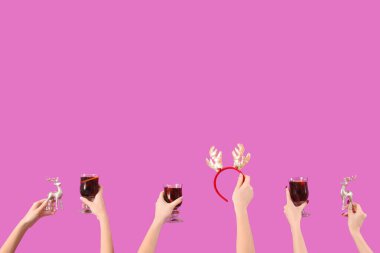 Sıcak şarap kadehleriyle kadın elleri ve pembe arka planda Noel dekoru.