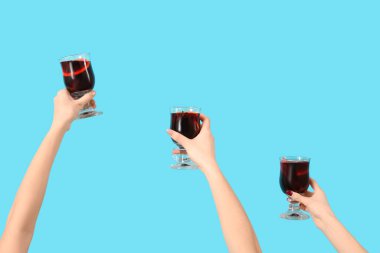 Mavi arka planda sıcak şarap kadehleriyle kadın elleri.