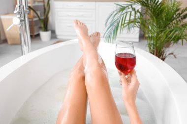 Bir bardak şarapla evde banyo yapan genç bir kadın, yakın plan.