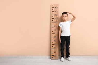 Bej duvarın yanında boyunu ölçen sevimli küçük bir çocuk.