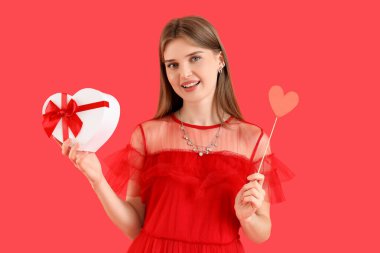 Kırmızı arka planda hediye kutusu ve kağıt kalpli güzel bir kadın. Sevgililer Günü kutlaması