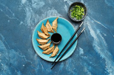 Lezzetli Çin jiaozi tabağı, yeşil soğan ve mavi arka planda sos.