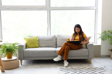 Ofisteki koltukta tabletle çalışan Asyalı iç mimar.