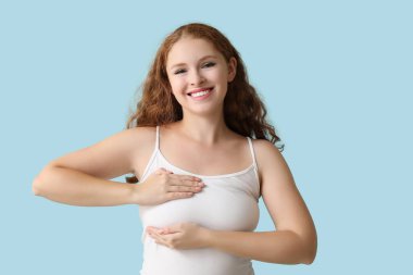 Mavi arka planda göğüslerini kontrol eden genç bir kadın. Kanser farkındalığı kavramı