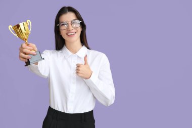 Altın bardaklı genç bir iş kadını leylak arka planda baş parmak gösteriyor.