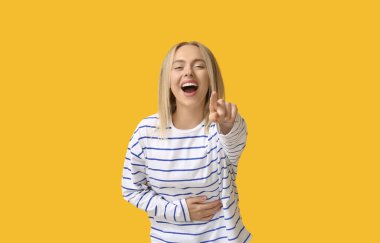 Güzel, mutlu, genç bir kadın sarı arka plandaki izleyiciyi işaret ediyor.