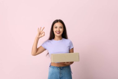 Paketi olan güzel genç bir bayan pembe arka planda güzel bir jest yapıyor.