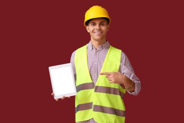 Genç erkek mühendis kırmızı arkaplanda boş ekranlı tablet bilgisayarını işaret ediyor
