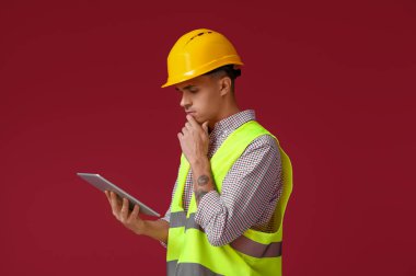 Kırmızı arka planda tablet bilgisayarı olan genç erkek mühendis