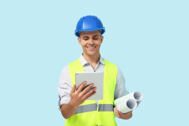 Mavi arka planda taslak ve tablet bilgisayarı olan genç erkek mühendis.