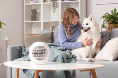 Evde Samoyed köpeği ve elektrikli fan ısıtıcısı olan genç bir kadın var.