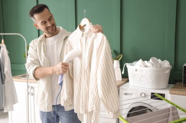 Çamaşır odasında buharlı gömlekli yakışıklı bir adam.