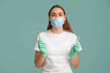 Mavi arka planda diş aletleri olan maskeli kadın dişçi. Dünya Diş Hekimi Günü