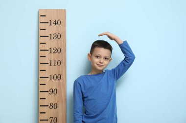 Mavi arka planda boyunu ölçen sevimli küçük bir çocuk.