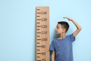 Mavi arka planda boyunu ölçen sevimli küçük bir çocuk.