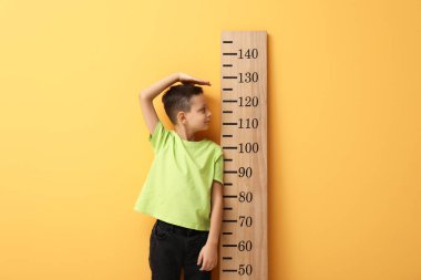 Sarı arka planda boyunu ölçen sevimli küçük bir çocuk.