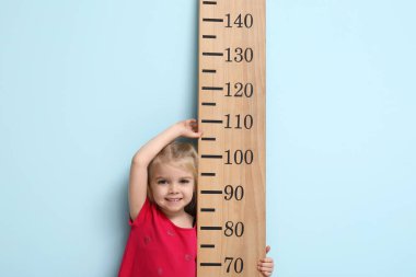 Mavi arka planda boyunu ölçen tatlı küçük bir kız.