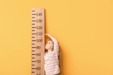 Sarı arka planda boyunu ölçen tatlı küçük bir kız.