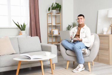 Evde koltukta, dizüstü bilgisayar kullanan genç adam