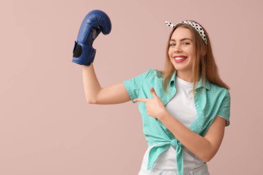 Mutlu genç kadın pembe arka planda boks eldivenini işaret ediyor.