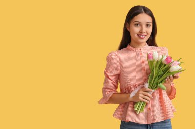 Sarı arka planda güzel lalelerle dolu buketi olan mutlu genç Asyalı kadın. Uluslararası Kadınlar Günü