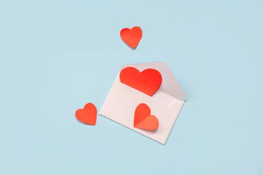 Mavi zemin üzerinde kağıt kalpler ve zarf olan kompozisyon. Sevgililer Günü kutlaması