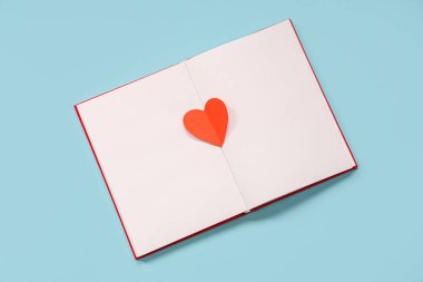 Mavi arka planda kağıt kalpli boş bir kitap. Sevgililer Günü kutlaması