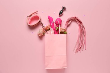 Güzel gül çiçekleri ve pembe arka planda farklı seks oyuncakları olan kağıt torba.