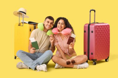 Sarı arka planda bavulları ve pasaportları olan iki turist.