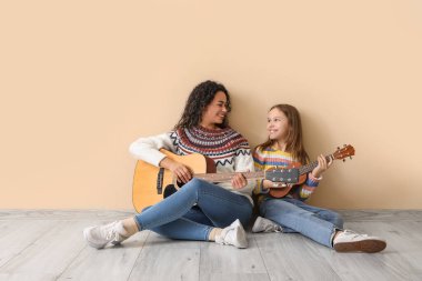 Genç kadın ve kız bej arka planda birlikte akustik gitar çalıyorlar.