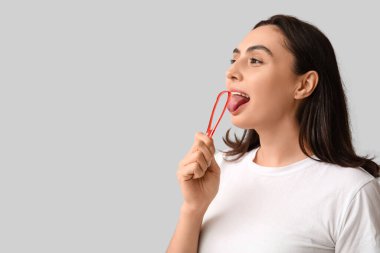 Young woman using tongue scraper on light background, closeup