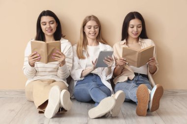 Bej duvarın yanında kitapları ve tablet bilgisayarı olan kadınlar