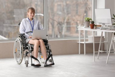 Young businesswoman in wheelchair working with laptop at office
