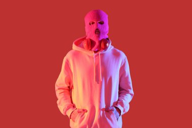 Kırmızı arka planda kulaklıkları olan kar maskeli yakışıklı bir genç.