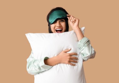 Pijamalı ve kahverengi arka planda yumuşak yastıklı güzel bir kadın.