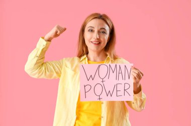 Elinde pembe arka planda mesaj yazan olgun bir kadın elinde kağıt tutuyor.