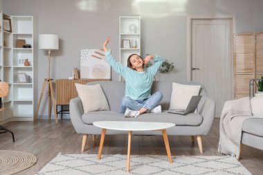 Young woman stretching on grey couch in living room
