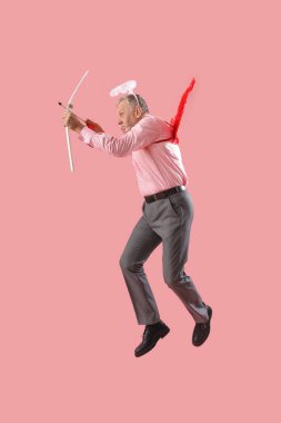 Aşk tanrısı gibi giyinmiş olgun bir adamın pembe arka planda ok atması. Sevgililer Günü kutlaması