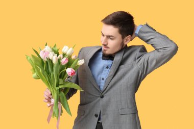 Sarı arka planda bir buket güzel lalesi olan düşünceli genç bir adam. Uluslararası Kadınlar Günü