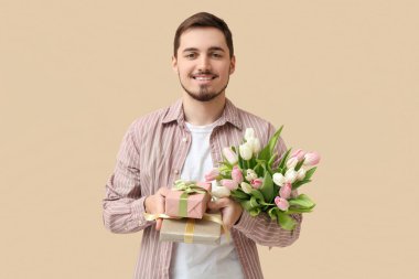 Güzel lalelerle dolu buketi ve bej arka planda hediye kutuları olan genç bir adam. Uluslararası Kadınlar Günü