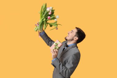 Güzel lalelerden oluşan buketi ve sarı arka planda hediye kutusu olan genç bir adam. Uluslararası Kadınlar Günü