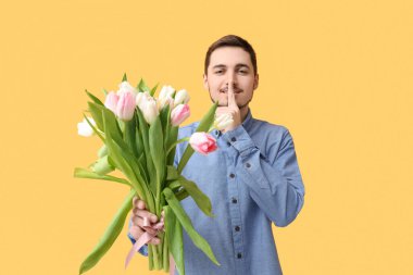 Bir buket güzel laleli genç adam sarı arka planda sessizlik jesti gösteriyor. Uluslararası Kadınlar Günü