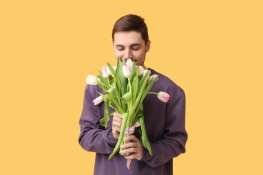 Sarı arka planda güzel lalelerle dolu bir buketi olan genç adam. Uluslararası Kadınlar Günü