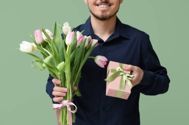 Bir buket güzel lalesi ve yeşil arka planda hediye kutusu olan genç bir adam. Uluslararası Kadınlar Günü
