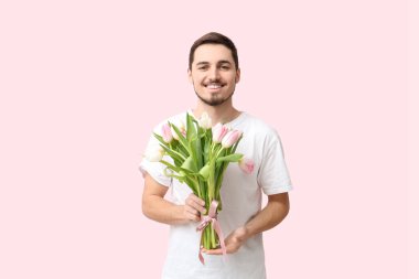 Pembe arka planda güzel lalelerle dolu buketi olan mutlu genç bir adam. Uluslararası Kadınlar Günü