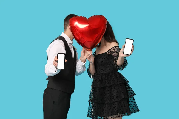 Young couple with mobile phones and heart-shaped air balloon on blue background. Online dating
