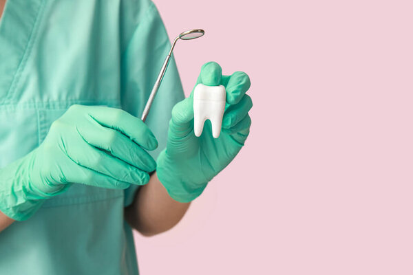 Dentist with dental mirror and tooth model on pink background, closeup. World Dentist Day