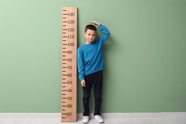 Милый маленький мальчик, измеряющий высоту возле зеленой стены